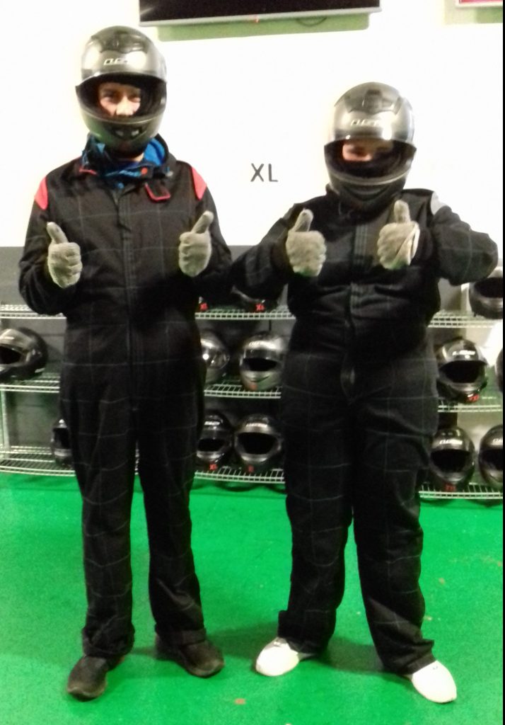 Photo of a youth worker and a young person dressed for go-karting with their thumbs up.