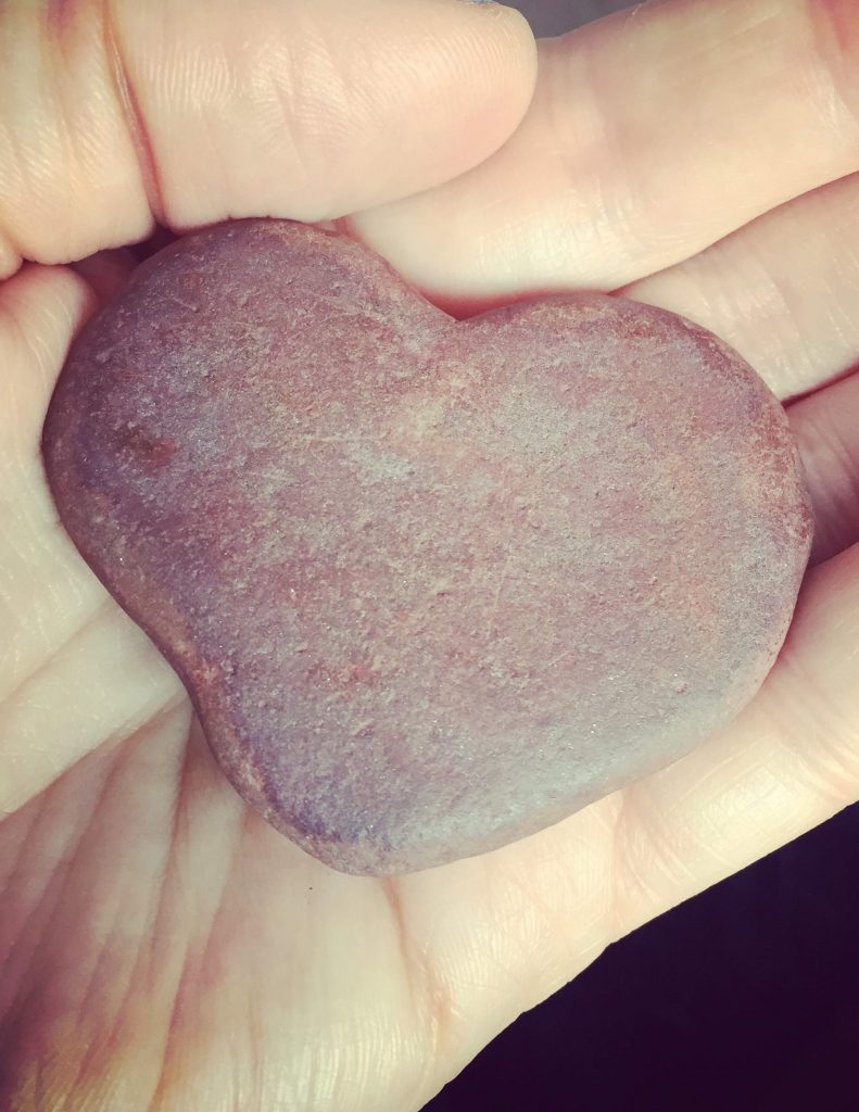 Hand holding a pink or red heart shaped stone.